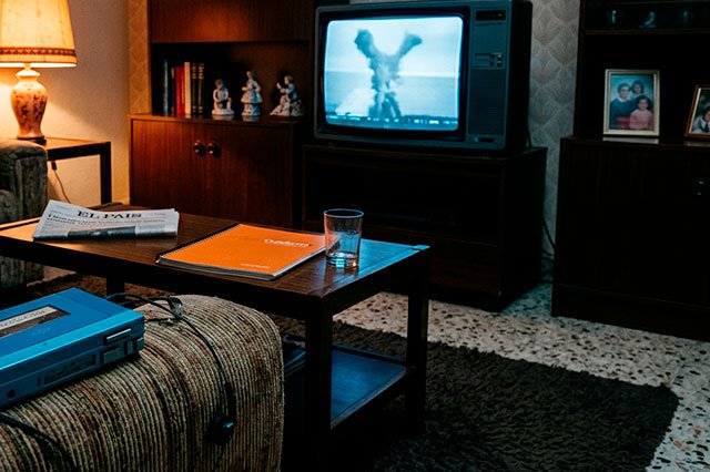 Walkman azul ochentero sobre un sofá iluminado por la luz fría de una televisión que muestra una forma abstracta de humo en Y